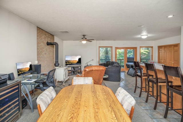 dining space with a wood stove, visible vents, ceiling fan, and a textured ceiling