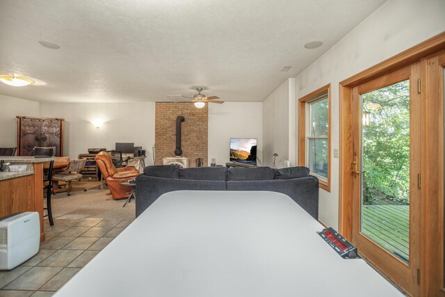 living room featuring a textured ceiling, light tile patterned flooring, a wood stove, and a ceiling fan