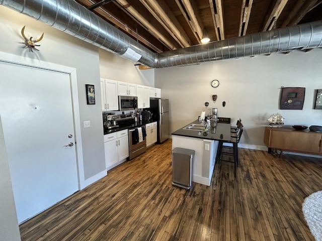 kitchen featuring stainless steel appliances, a breakfast bar, dark countertops, and white cabinetry