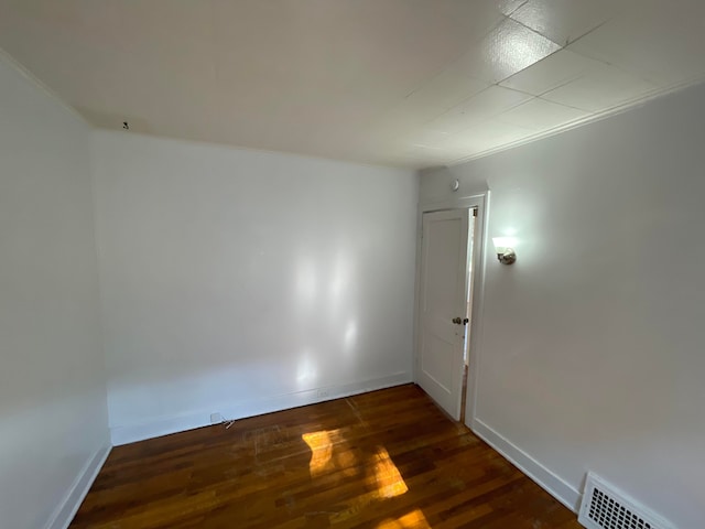 empty room with baseboards, visible vents, and dark wood finished floors