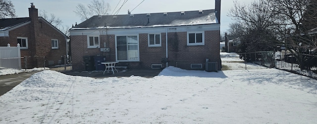 snow covered property with brick siding and fence