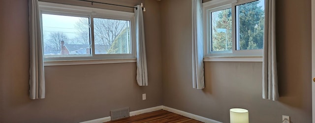 unfurnished room featuring wood finished floors, visible vents, and baseboards