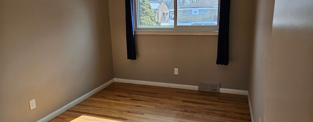 spare room with wood finished floors, visible vents, and baseboards