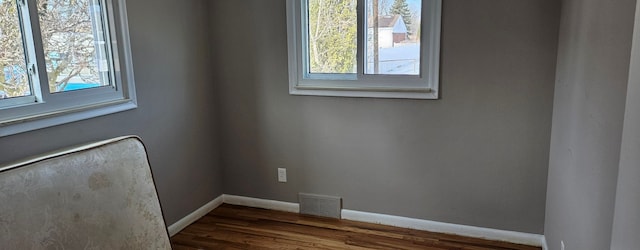 unfurnished room with dark wood-type flooring, visible vents, and baseboards