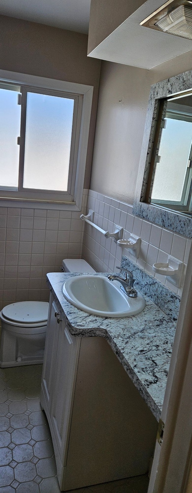 half bath featuring toilet, tile patterned flooring, vanity, and tile walls