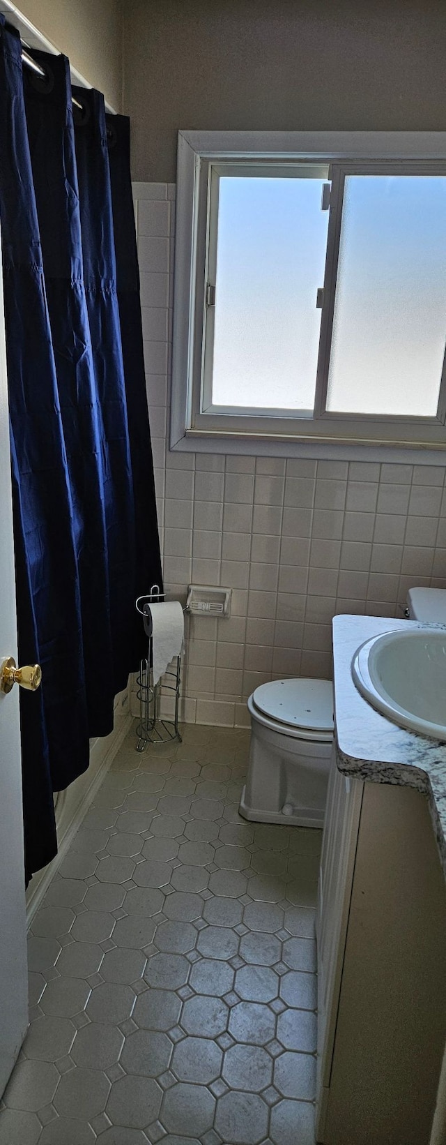 full bath with curtained shower, tile walls, vanity, and toilet