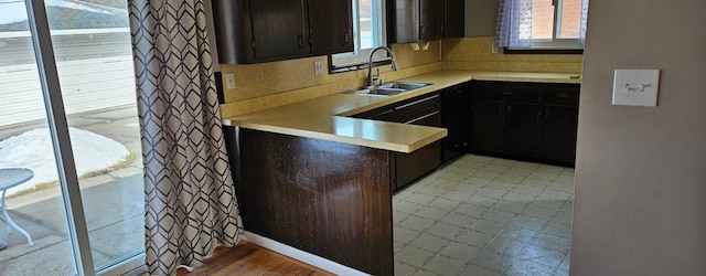 kitchen featuring a peninsula, dark brown cabinets, light countertops, and a sink