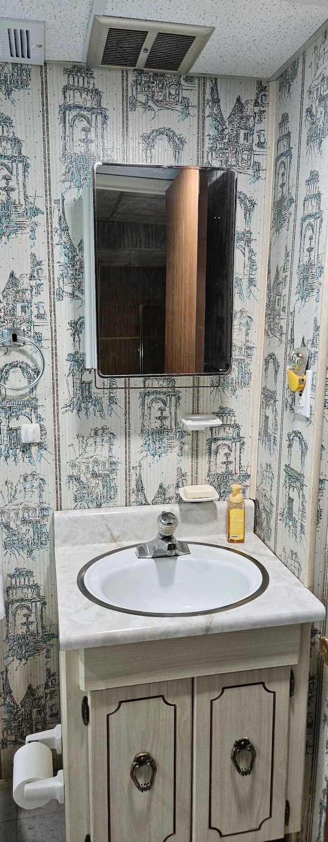 bathroom with wallpapered walls, a textured ceiling, and vanity