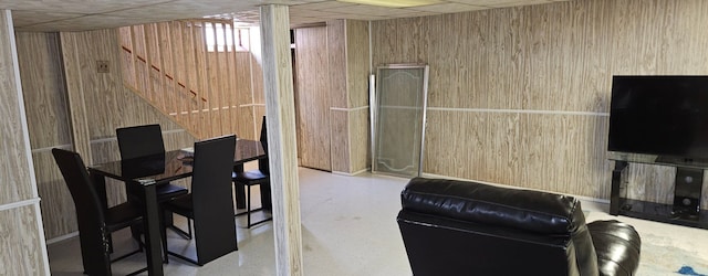 dining area with stairway, a drop ceiling, and wooden walls