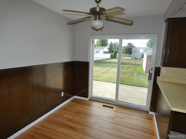 doorway to outside featuring light wood finished floors, visible vents, a ceiling fan, wainscoting, and wooden walls