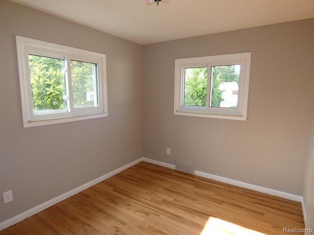 spare room with a wealth of natural light, visible vents, light wood finished floors, and baseboards