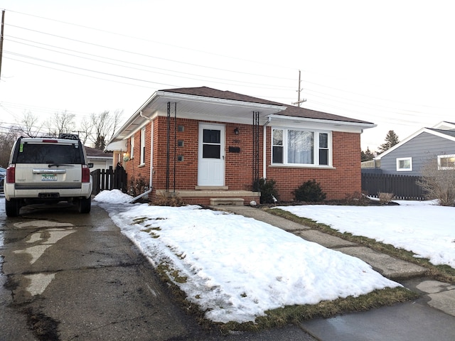 bungalow featuring driveway, fence, and brick siding