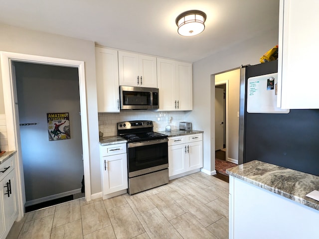 kitchen featuring stainless steel appliances, tasteful backsplash, white cabinetry, light stone countertops, and baseboards