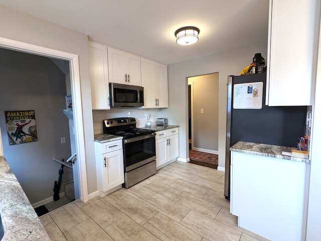 kitchen with tasteful backsplash, appliances with stainless steel finishes, white cabinets, and light stone counters