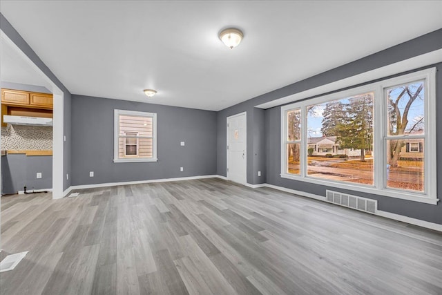 unfurnished living room featuring light wood-style floors, visible vents, and baseboards