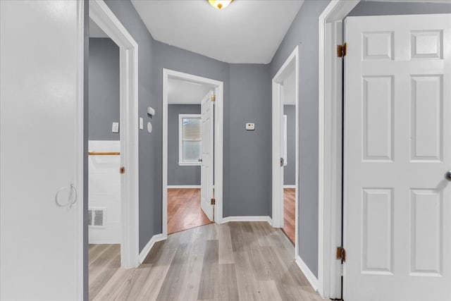 corridor featuring visible vents, light wood-style flooring, and baseboards