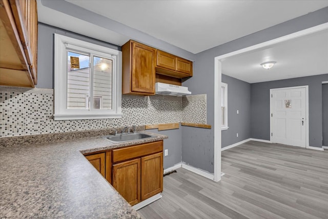 kitchen with light wood-style flooring, brown cabinets, a sink, and under cabinet range hood