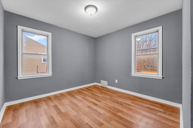 empty room with light wood-style flooring, visible vents, and baseboards