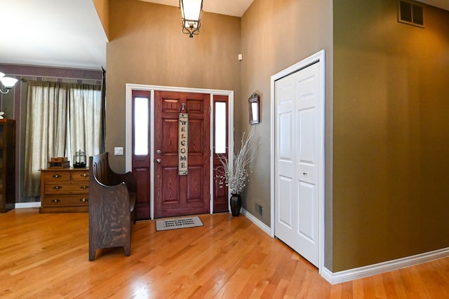 entrance foyer with a towering ceiling, wood finished floors, visible vents, and baseboards