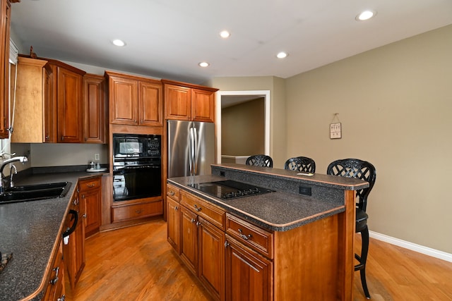 kitchen with a breakfast bar, light wood finished floors, dark countertops, a sink, and black appliances