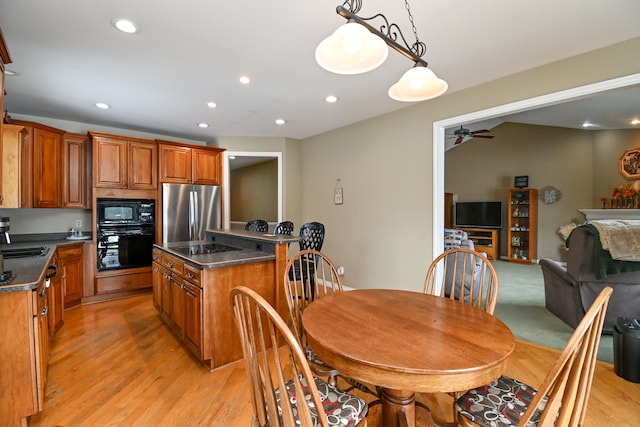 kitchen featuring a center island, light wood-style floors, brown cabinets, black appliances, and dark countertops