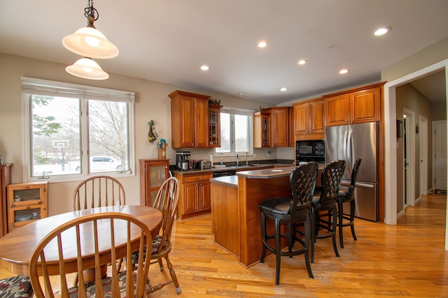 kitchen featuring brown cabinetry, dark countertops, freestanding refrigerator, black microwave, and a sink