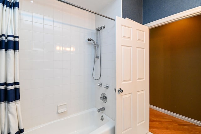 full bathroom with wallpapered walls, wood finished floors, shower / bath combo with shower curtain, and baseboards