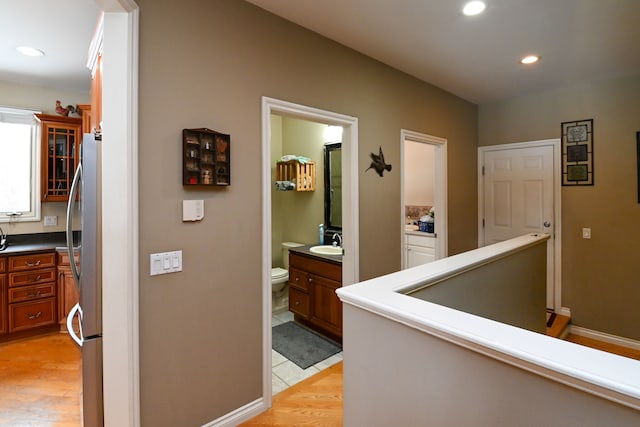 hall featuring baseboards, an upstairs landing, light wood-style floors, a sink, and recessed lighting