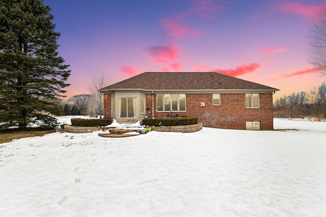 snow covered back of property with brick siding