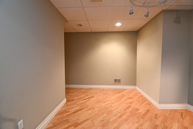 empty room featuring baseboards, visible vents, a drop ceiling, and light wood finished floors