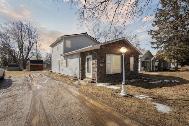 view of front of home featuring driveway, stone siding, a shed, and an outbuilding