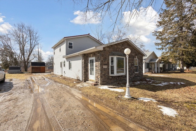 view of front of home with driveway, a storage shed, stone siding, and an outbuilding