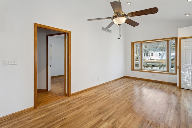 spare room featuring light wood-style floors, baseboards, visible vents, and vaulted ceiling