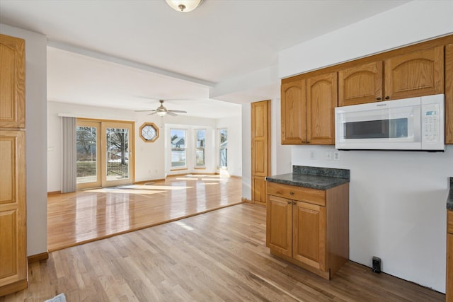 kitchen featuring open floor plan, white microwave, light wood finished floors, and dark countertops