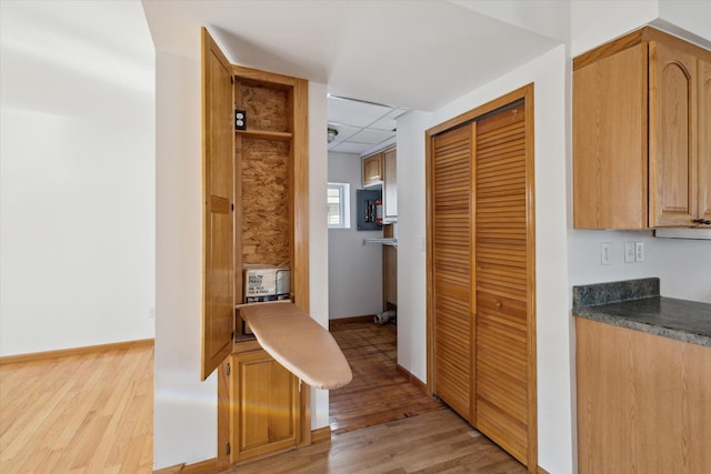 corridor with a paneled ceiling, light wood finished floors, and baseboards