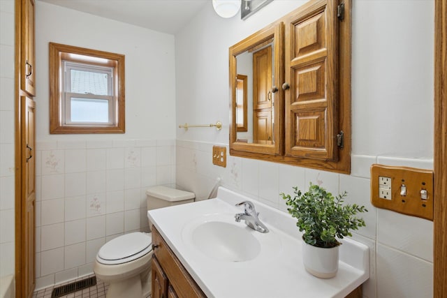 bathroom with toilet, vanity, visible vents, tile walls, and wainscoting