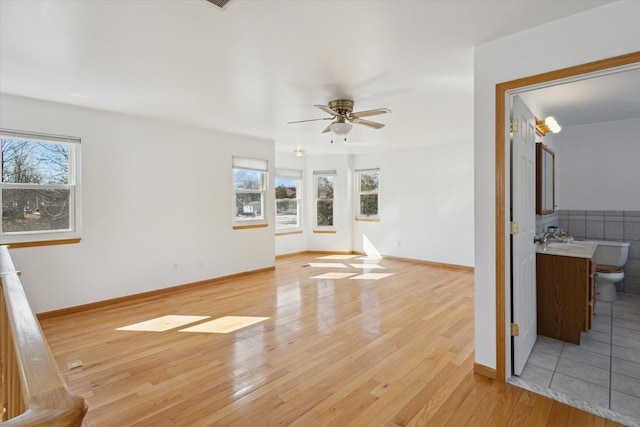 unfurnished living room featuring light wood finished floors, baseboards, and a ceiling fan