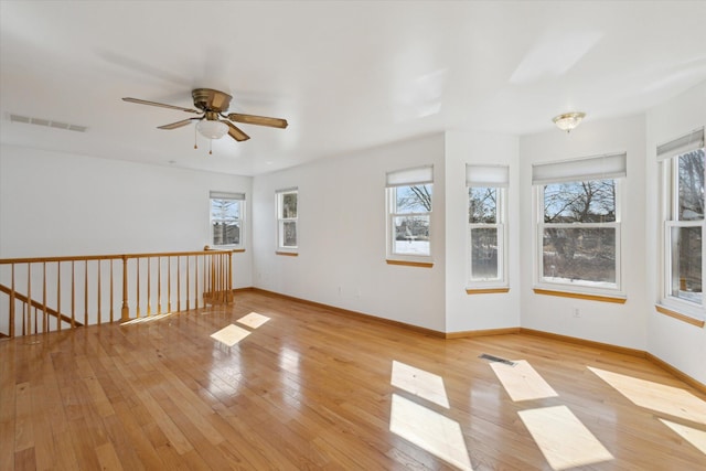 empty room featuring a ceiling fan, light wood-type flooring, visible vents, and baseboards