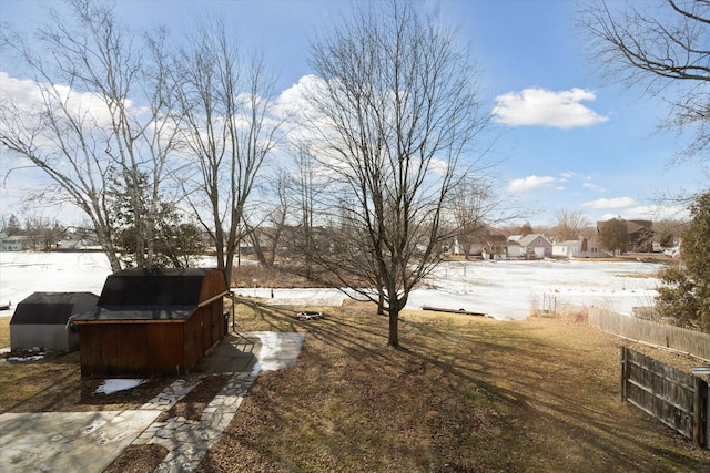 yard covered in snow featuring a storage shed, an outdoor structure, and fence