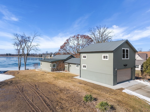 view of front of property with driveway, metal roof, a water view, an attached garage, and a front lawn