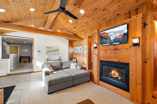 living area featuring vaulted ceiling with beams, light colored carpet, a glass covered fireplace, wood walls, and wooden ceiling