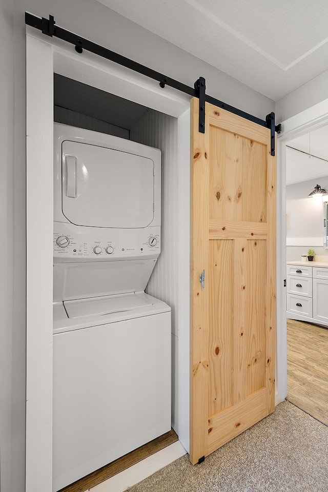 washroom featuring laundry area, a barn door, stacked washer / dryer, and carpet floors