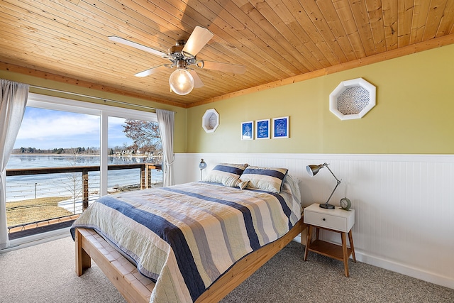 carpeted bedroom with a water view, wooden ceiling, a ceiling fan, and a wainscoted wall