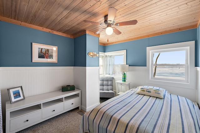 carpeted bedroom with wood ceiling, wainscoting, and ceiling fan