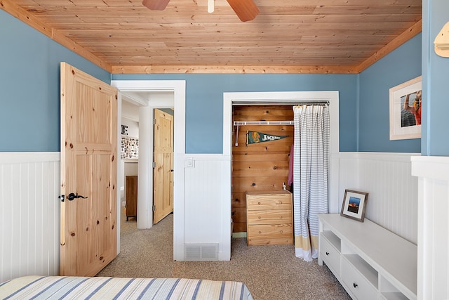 unfurnished bedroom featuring light carpet, wainscoting, and wooden ceiling