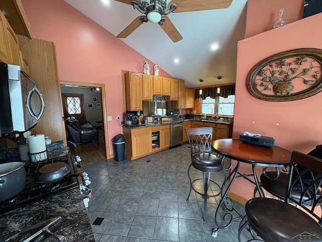 kitchen featuring stainless steel appliances, hanging light fixtures, a ceiling fan, dark stone countertops, and high vaulted ceiling