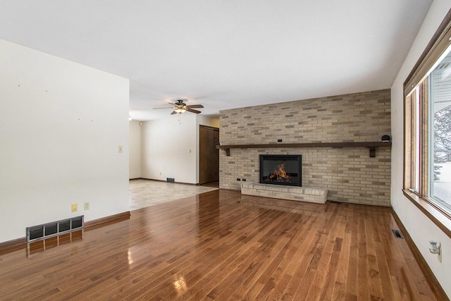 unfurnished living room featuring a brick fireplace, visible vents, and wood finished floors