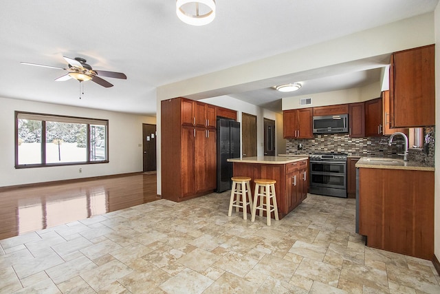 kitchen featuring backsplash, appliances with stainless steel finishes, a sink, a kitchen island, and a kitchen bar