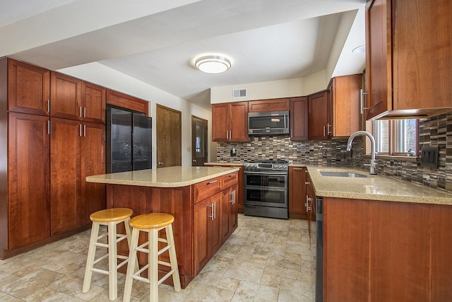 kitchen with visible vents, a kitchen island, stone finish floor, appliances with stainless steel finishes, and a sink