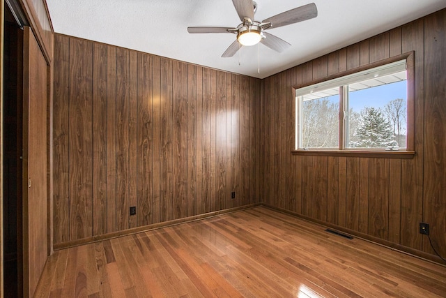 unfurnished room with visible vents, ceiling fan, wood walls, baseboards, and hardwood / wood-style flooring